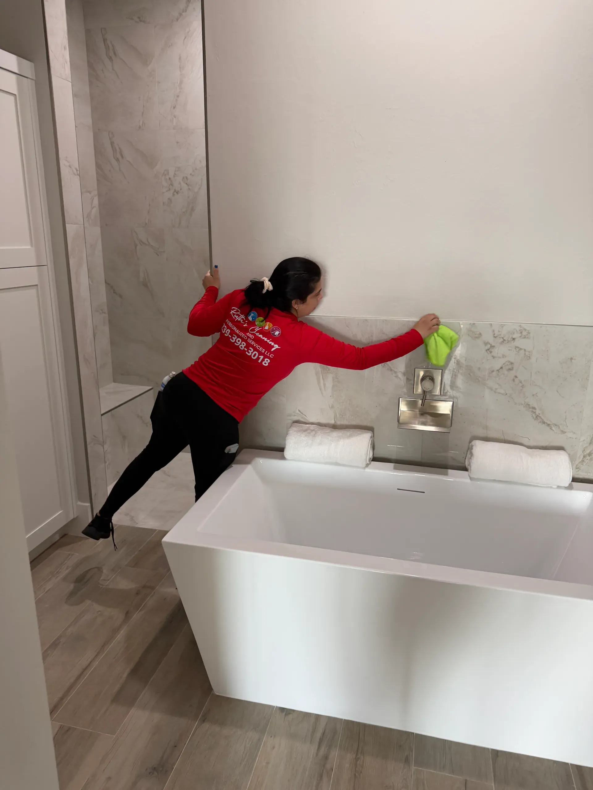 A team member leaning over a freestanding tub to wipe the marble backsplash with a green cloth
