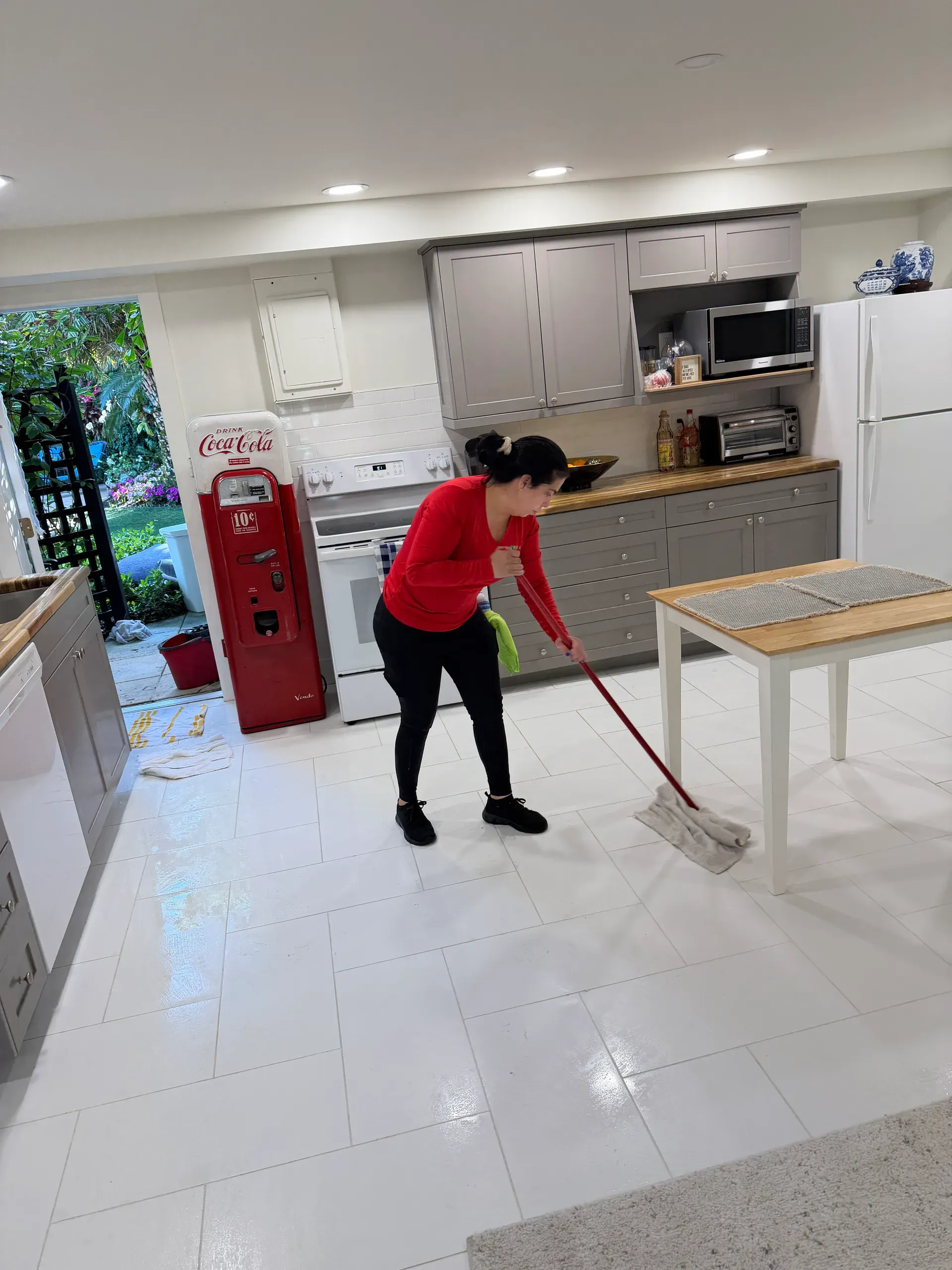 A team member mopping a white tile kitchen floor next to a vintage red Coca-Cola machine