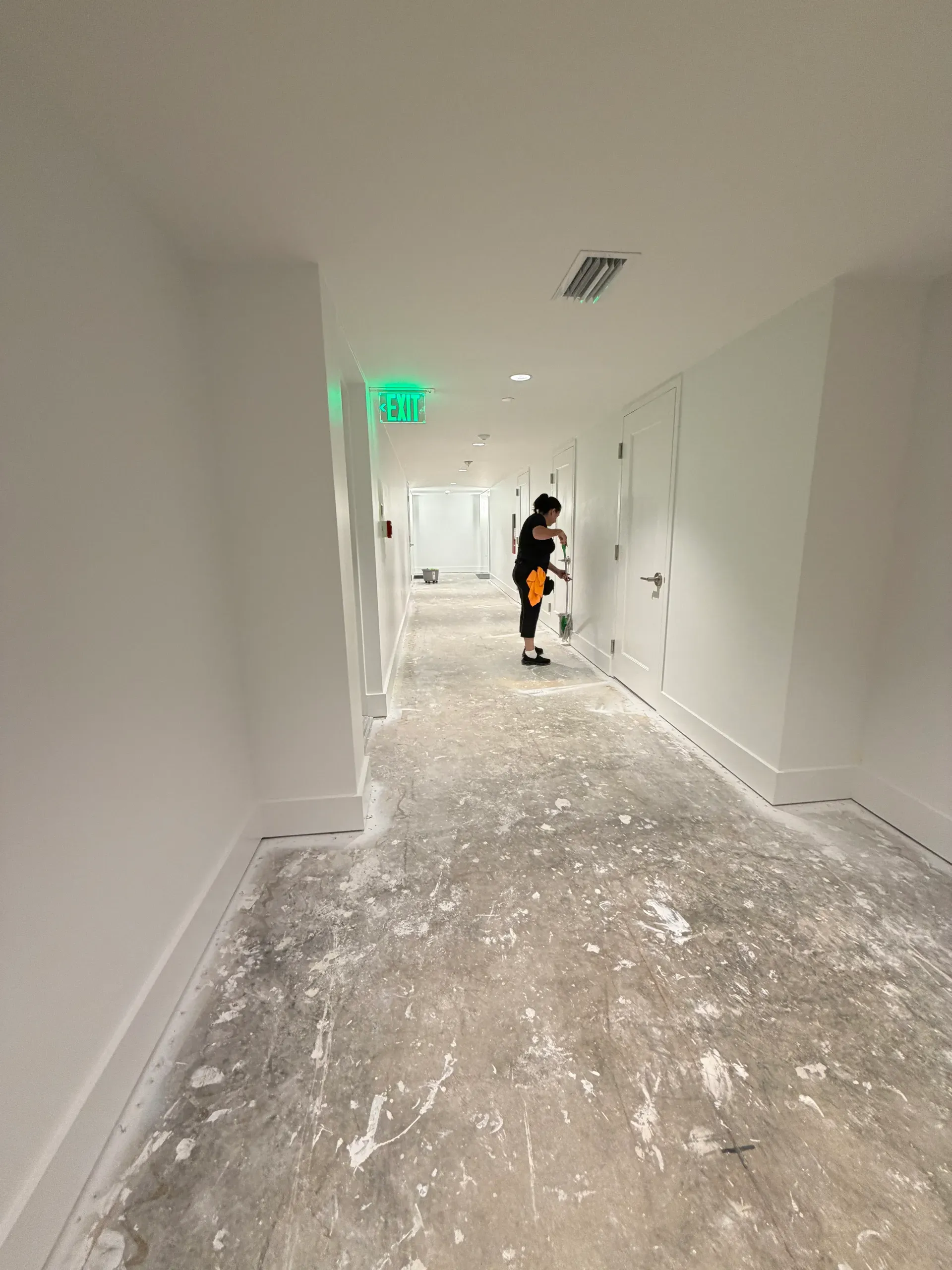 A team member cleaning a door in an unfinished building hallway with a paint-spattered concrete floor
