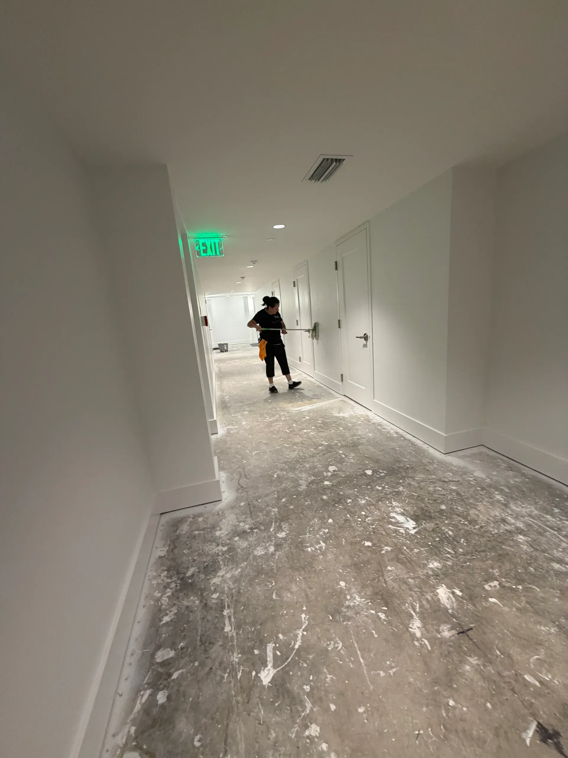 A team member using an extension pole on a door in an unfinished building hallway