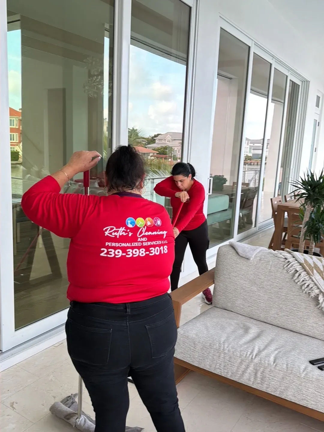 Two Ruth's Cleaning team members in red company shirts cleaning a waterfront lanai beside floor-to-ceiling sliding glass doors