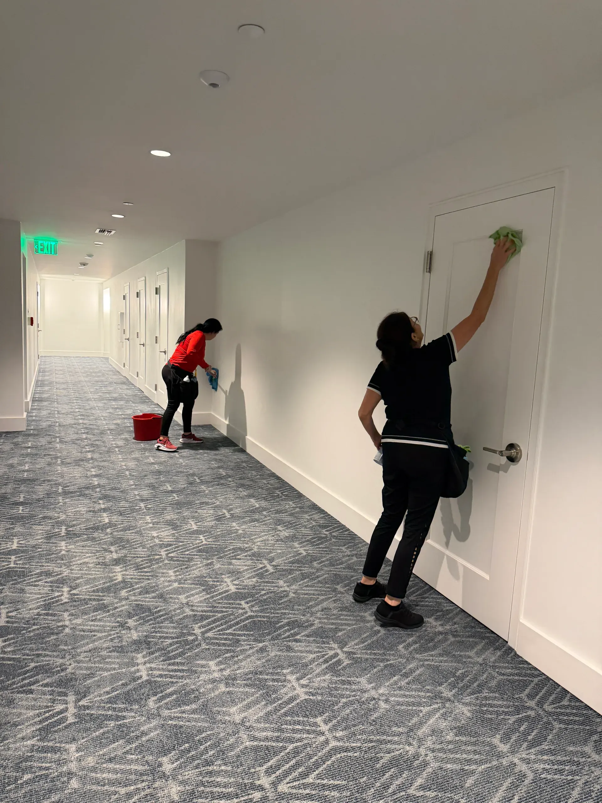 Two team members wiping doors and walls in a long carpeted building hallway