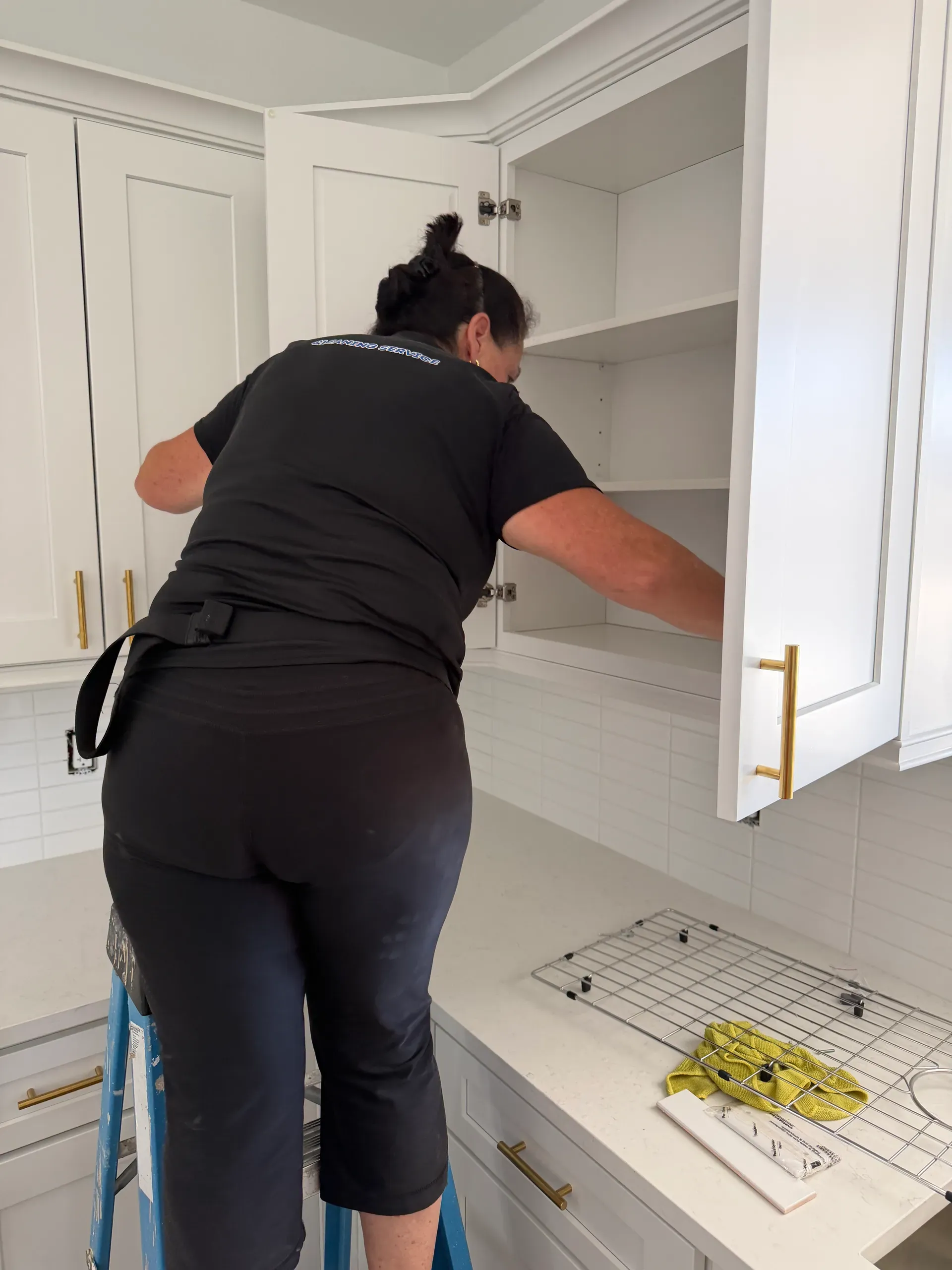 A team member on a step ladder reaching into an empty upper cabinet in a new white kitchen